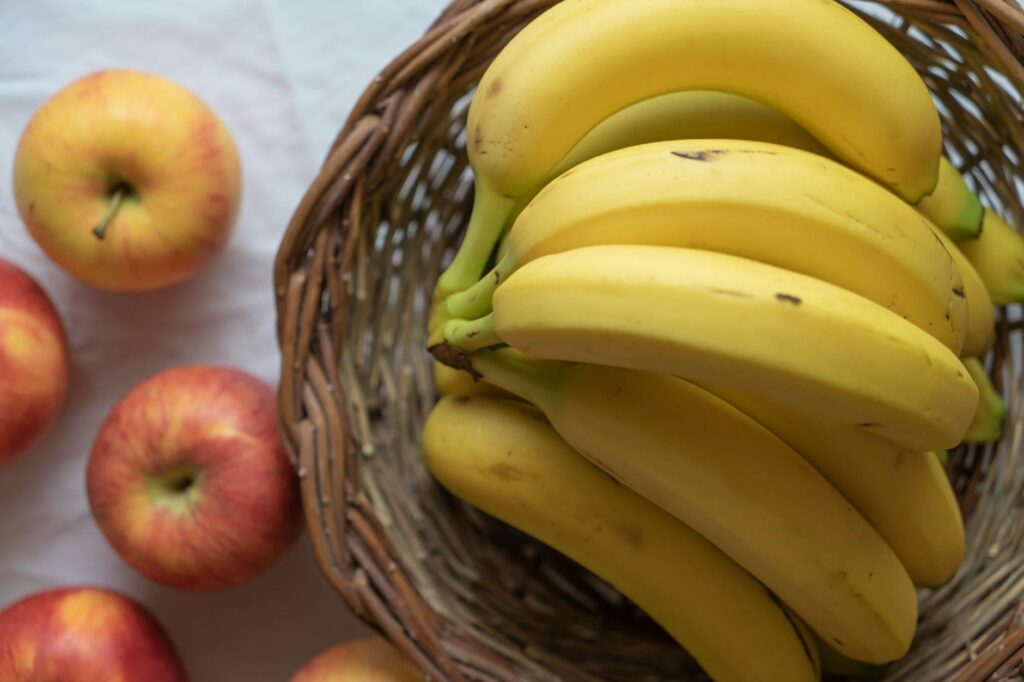 A close-up of ripe bananas in a wicker basket with apples on a white background.