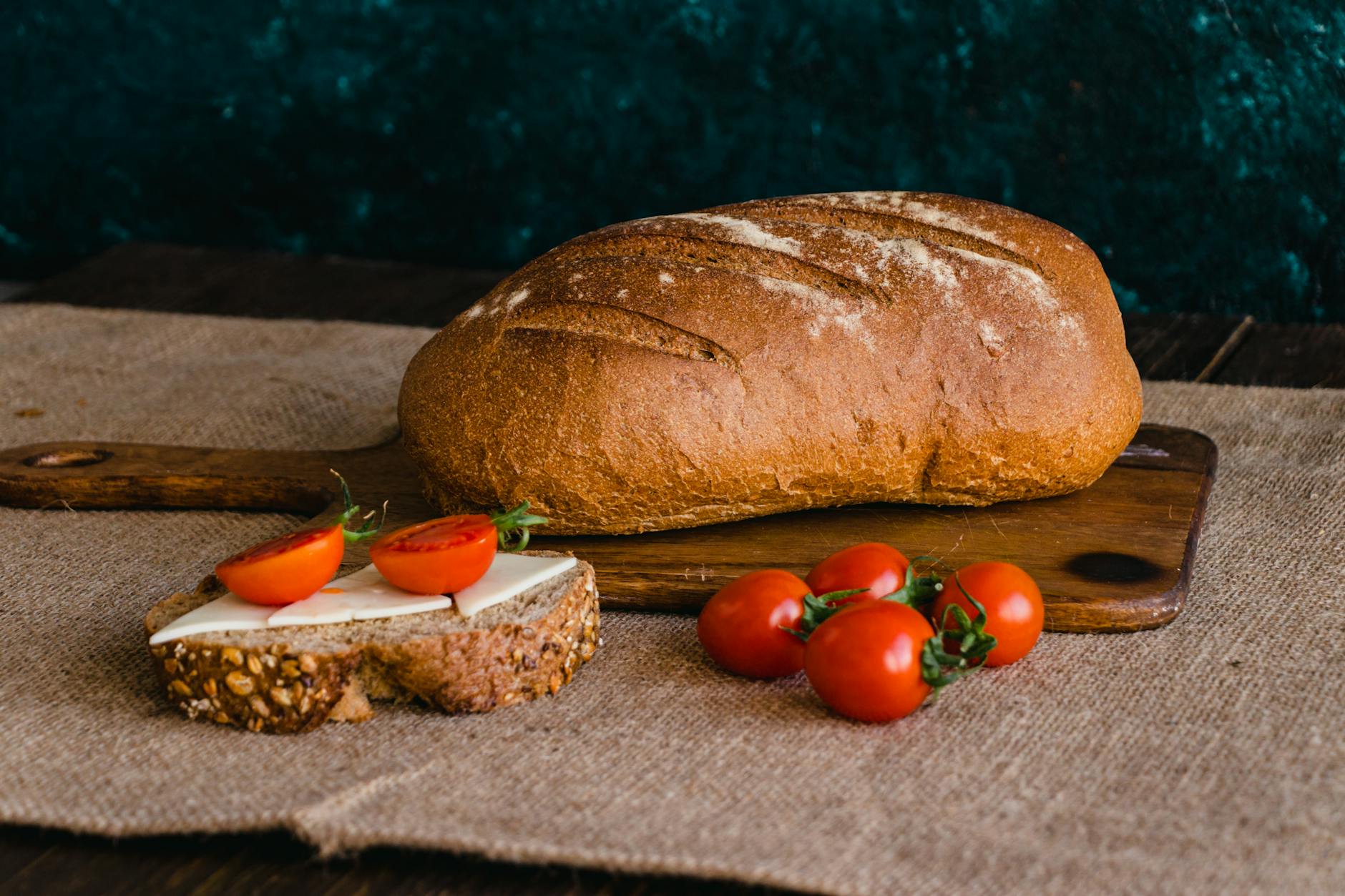 A delicious loaf of bread with cheese and cherry tomatoes, set on a rustic wooden board.