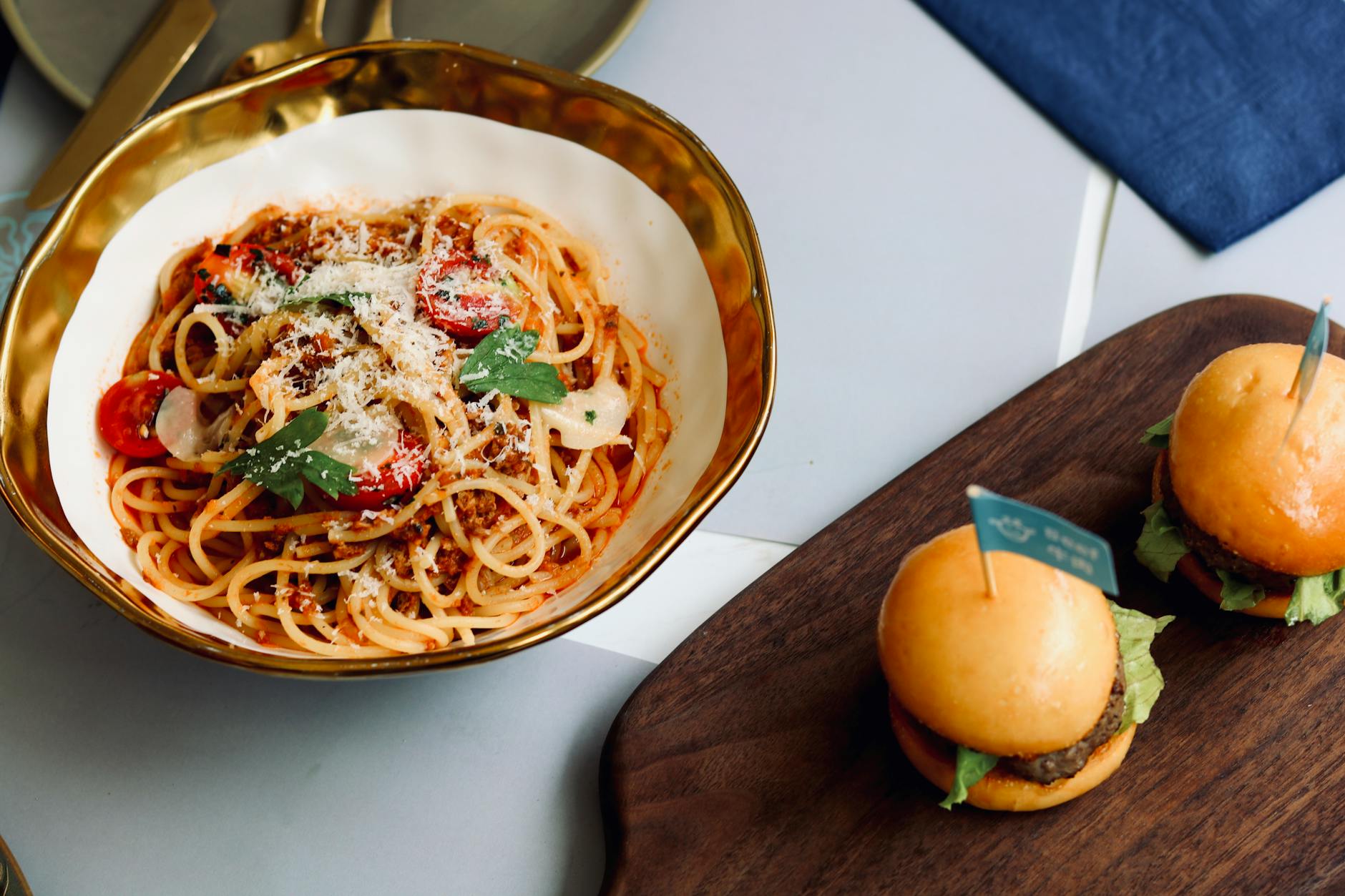 Close-up of delicious spaghetti with cherry tomatoes and mini burgers on a stylish table setting.