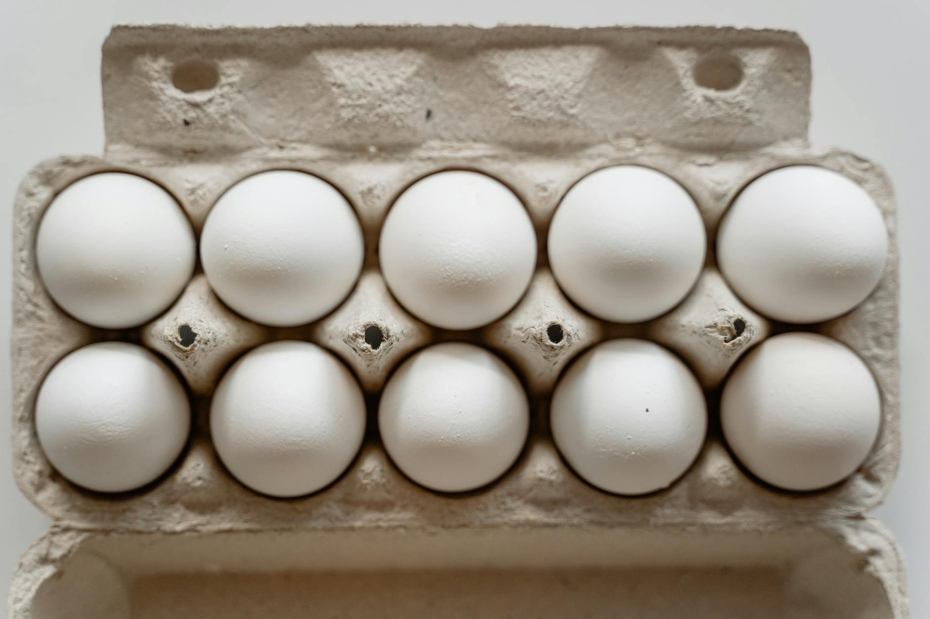 A dozen white eggs neatly arranged in a cardboard carton, viewed from above.