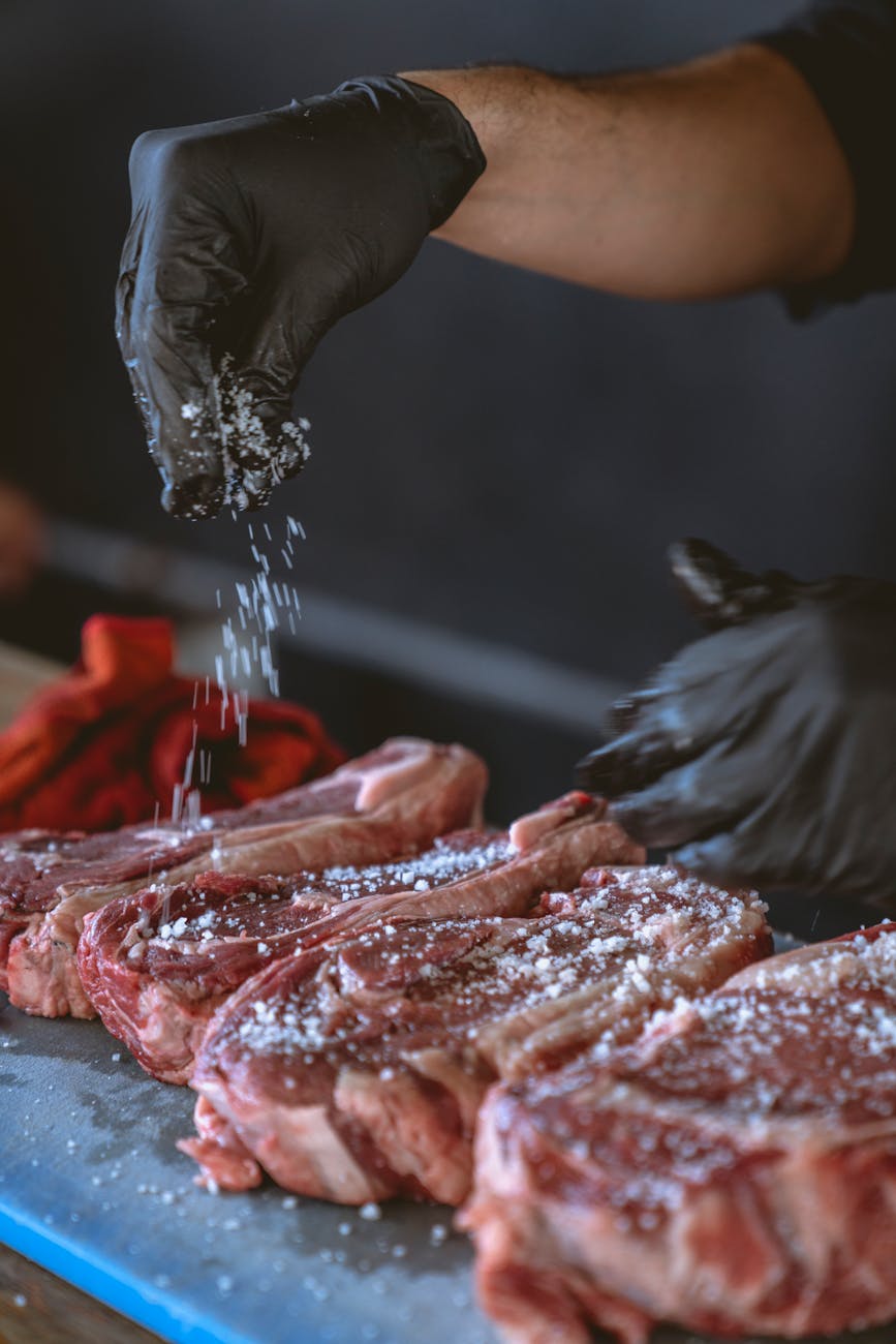 A chef seasons raw steaks with sea salt, perfecting the preparation process.