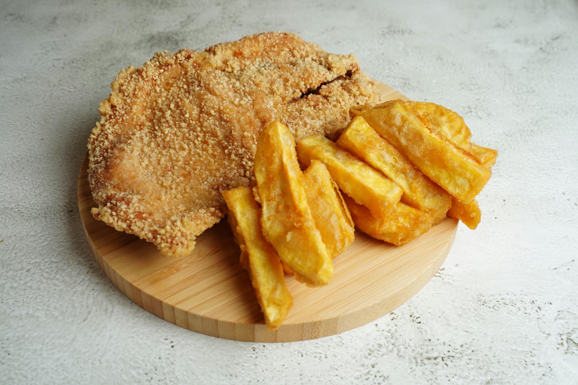 Crispy golden fried chicken served with chunky fries on a wooden board.