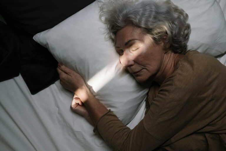 A serene moment of an elderly woman peacefully sleeping on a bed with soft lighting.